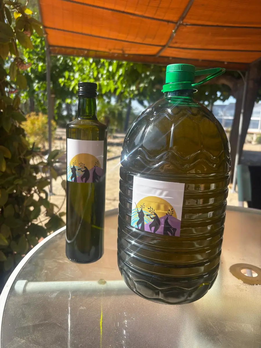 A bottle and a five-litre jug of our olive oil on a table under an orange awning